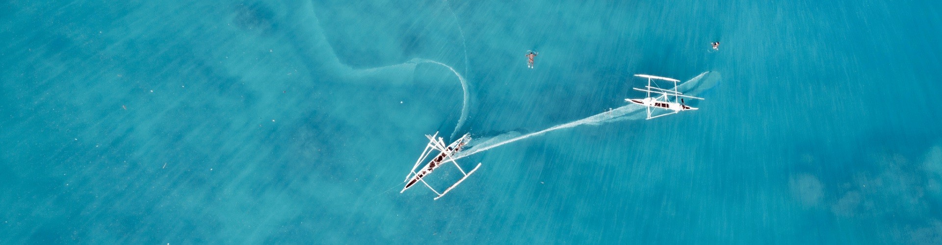 Aerial view of blue water with two boats and two swimmers