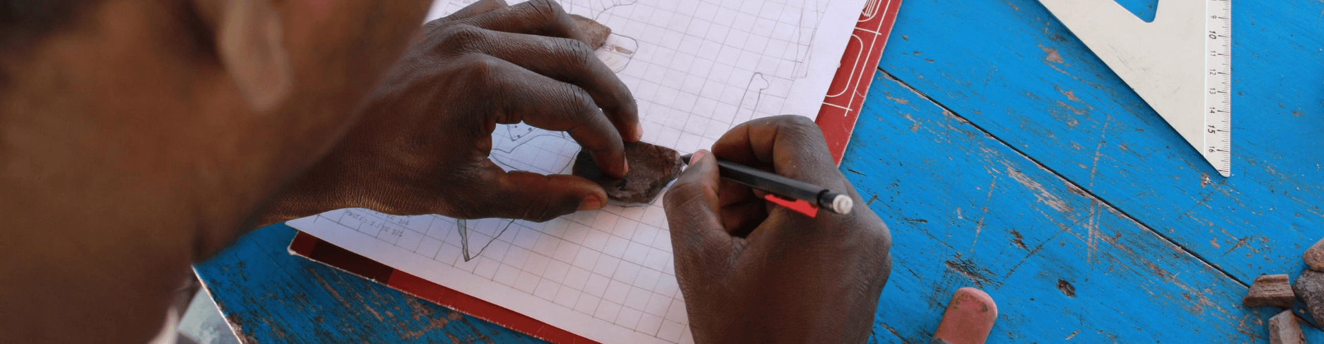Person tracing a rock on graph paper with drafting tools in the background