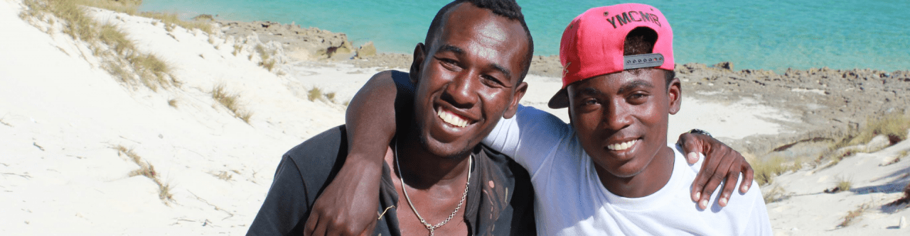 Two smiling people on the sand with their arms around each other's shoulder