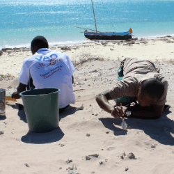 Two people working on the beach with water and boat in background